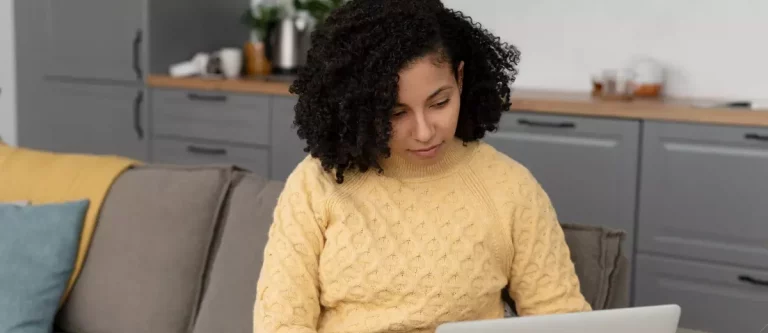 Mulher sentada em um sofá olhando para a tela do notebook