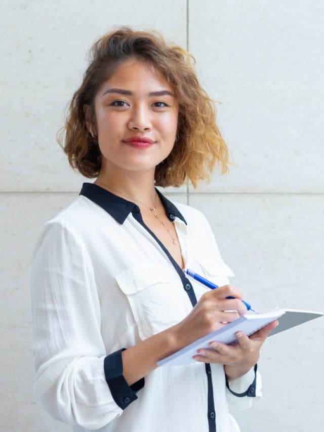 mulher asiática sorrindo enquanto escreve em um caderno