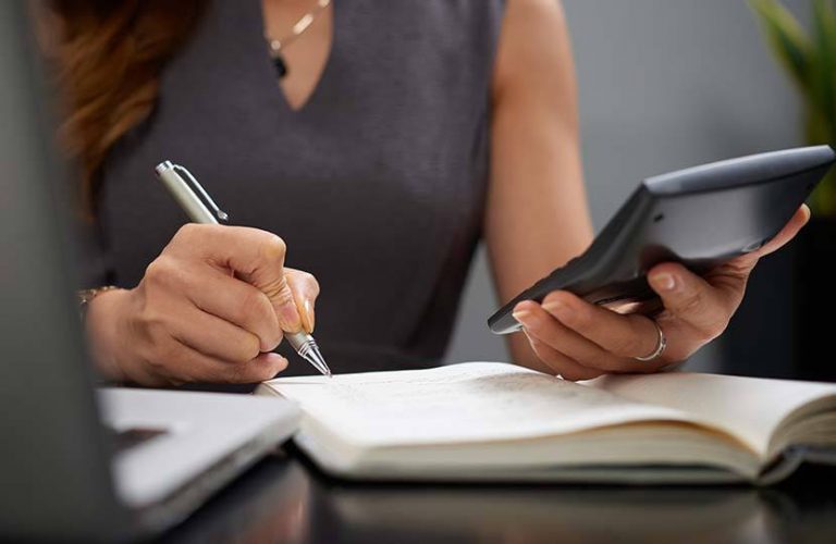 Cálculo de horas extras: mulher escreve no caderno enquanto olha a calculadora