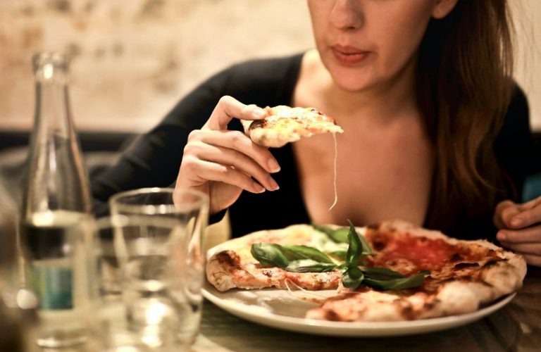 mulher branca comendo uma pizza em um restaurante