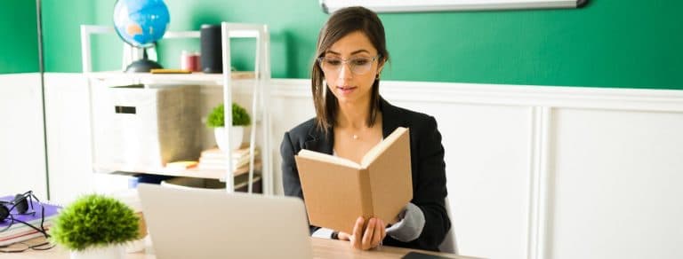 Mulher branca sentada em sala de aula e lendo um livro