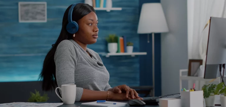 mulher sentada na mesa do computador, com fones de ouvindo