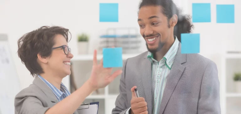 Homem e mulher sorrindo, colando post-its em um vidro