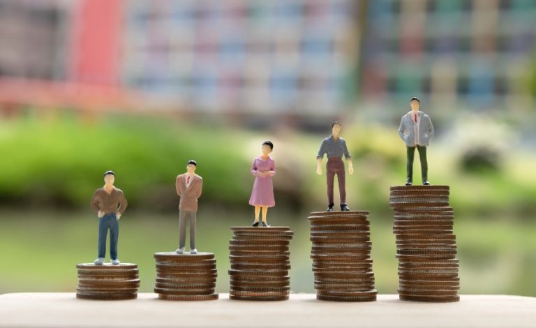 5 bonecas em cima de moedas empilhadas representando a desigualdade salarial