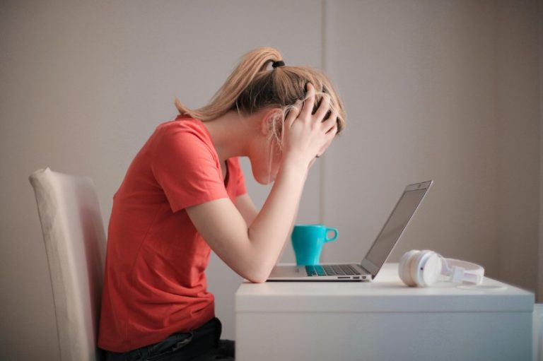 Mulher em frente ao computador com as mãos na cabeça com aspecto de preocupada.